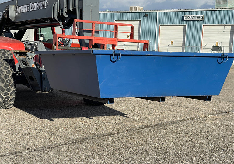 Blue steel washout pan attached to a vehicle on an asphalt surface with a building in the background.