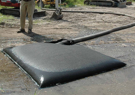 Large black oil absorbent pad on a construction site with a person and machinery in the background.