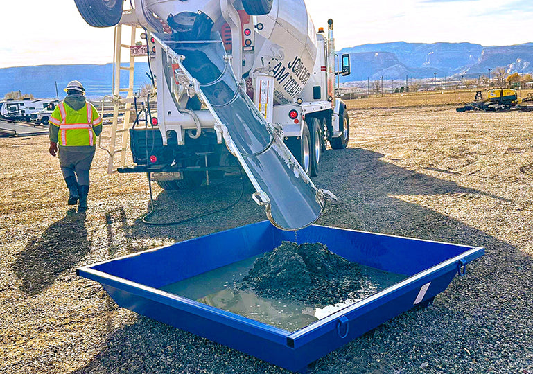 Cement truck pouring concrete into a blue pan with a worker observing.